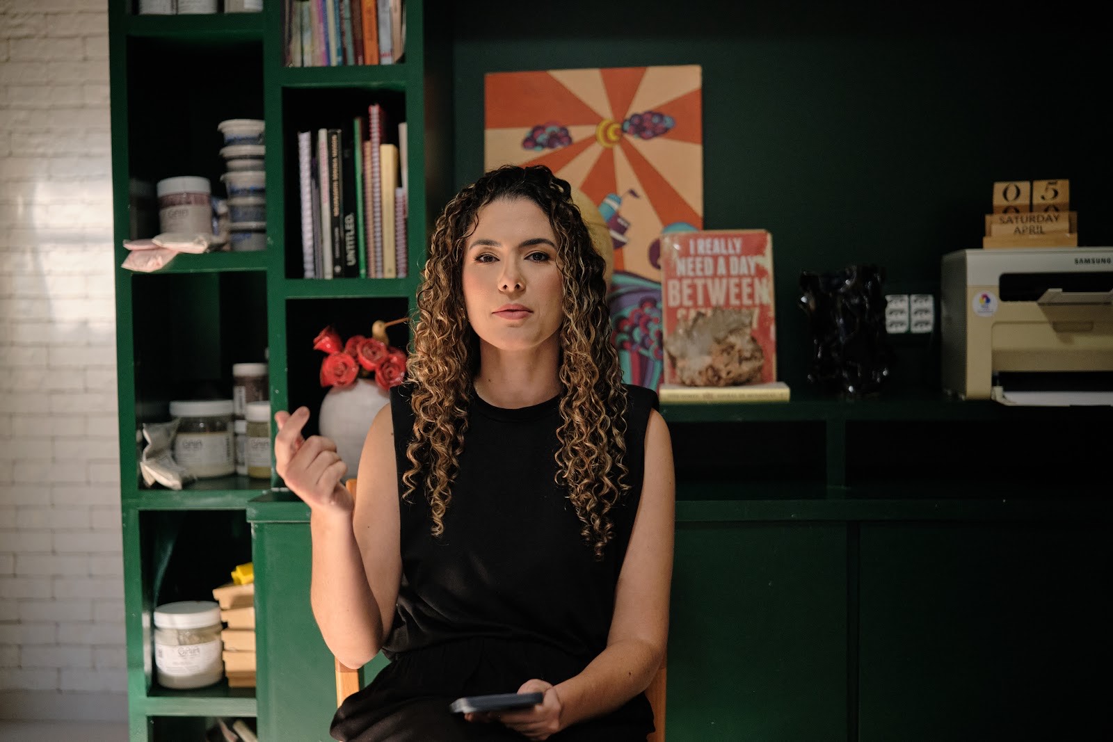 Isabela Malheiros no estúdio, em frente às prateleiras verdes